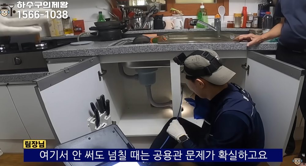 주방 싱크대 하부장을 열어 트랩과 배관 연결 상태를 확인하는 점검 장면