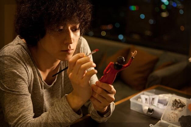 초인이 앉아서 피규어를 색칠하고 있습니다.