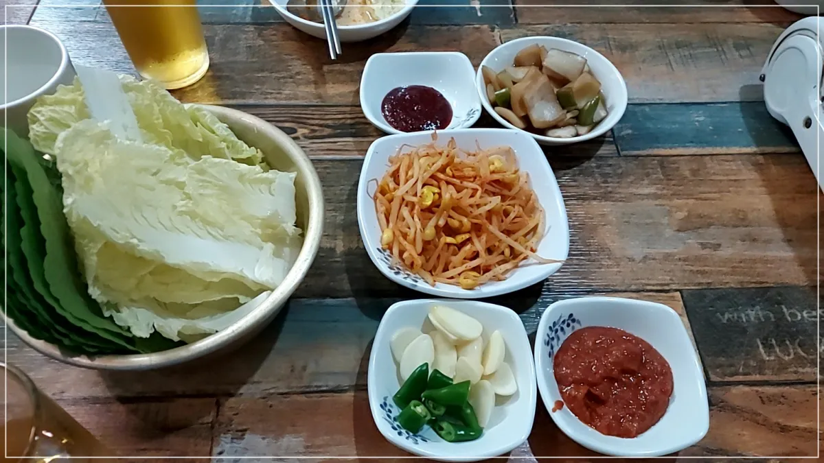 테이블 위 반찬, 배추쌈과 깻잎, 콩나물, 양파장아치, 마늘고추, 쌈장, 양념장, 맥주한잔