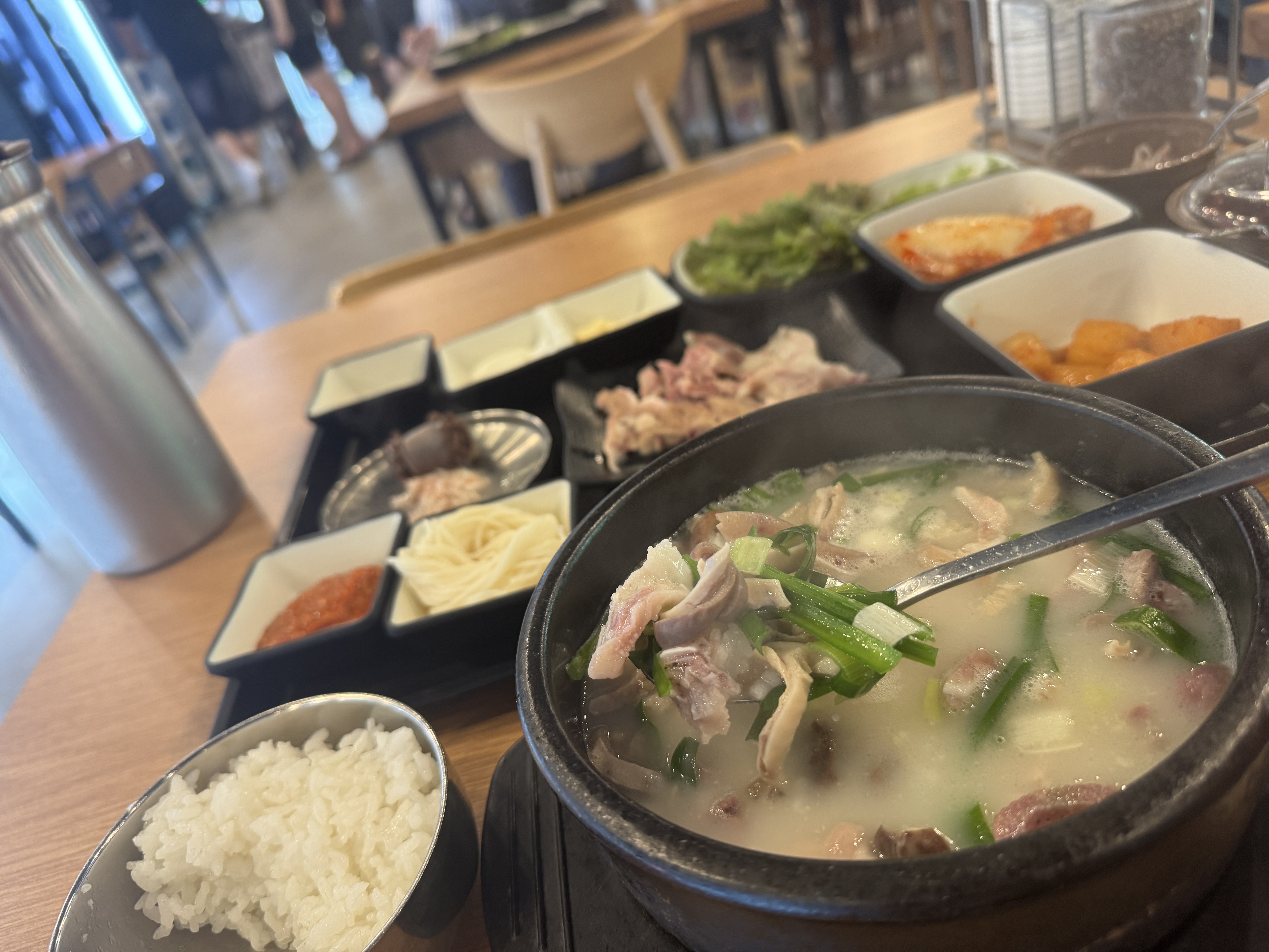 국밥 속 건더기와 흰 쌀밥을 함께 떠낸 숟가락 클로즈업. 뒤로는 수육과 밑반찬이 놓여 있다.