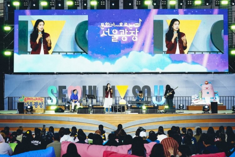 밤하늘을 배경으로 펼쳐진 문화가 흐르는 서울광장 무대, 대형 스크린에 여성 보컬 공연 모습이 실시간 송출되는 장면