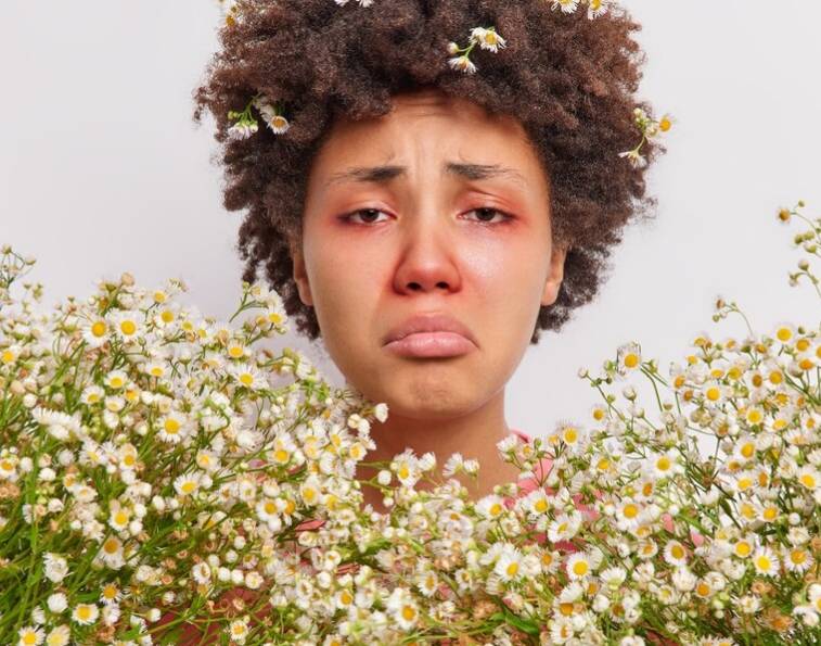 꽃에 둘러쌓여 비염에 때문에 고통스러워 하는 여성