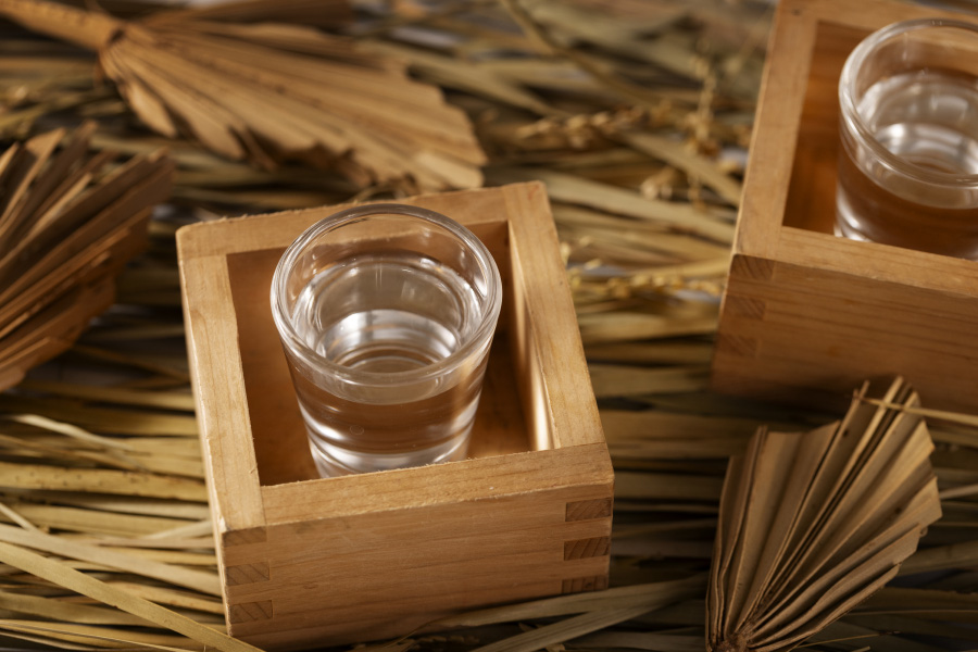 대나무 조각이 깔린 바닥에 네모난 나무 상자에 술이 가득한 투명한 소주잔 1잔을 넣은 것을 2개 놓아두고 찍은 사진