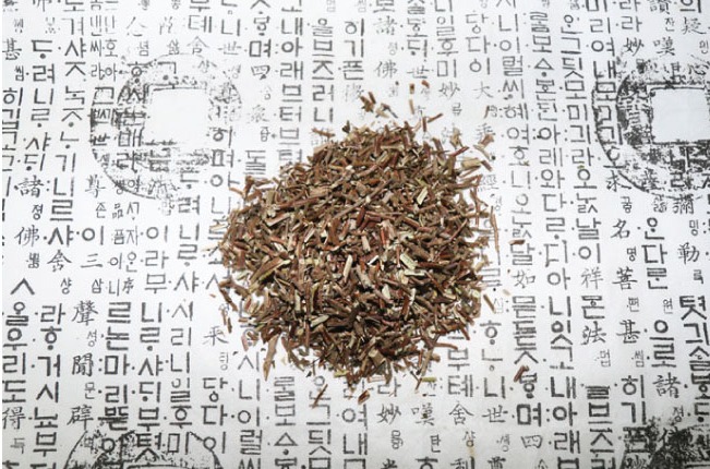 옛 글자가 새겨져 있는 하얀 종이 위에, 인동 풀의 줄기와 잎을 채취하여 잘 세척을 한 후에, 잘게 썰어 놓은 사진