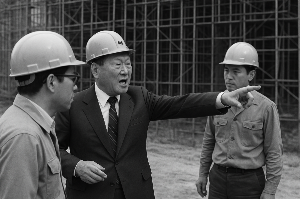 역동적인 흑백 사진. 건설 현장을 배경으로 안전모를 쓴 정주영 회장이 열정적으로 무언가를 지시하거나 직원들과 토론하는 모습