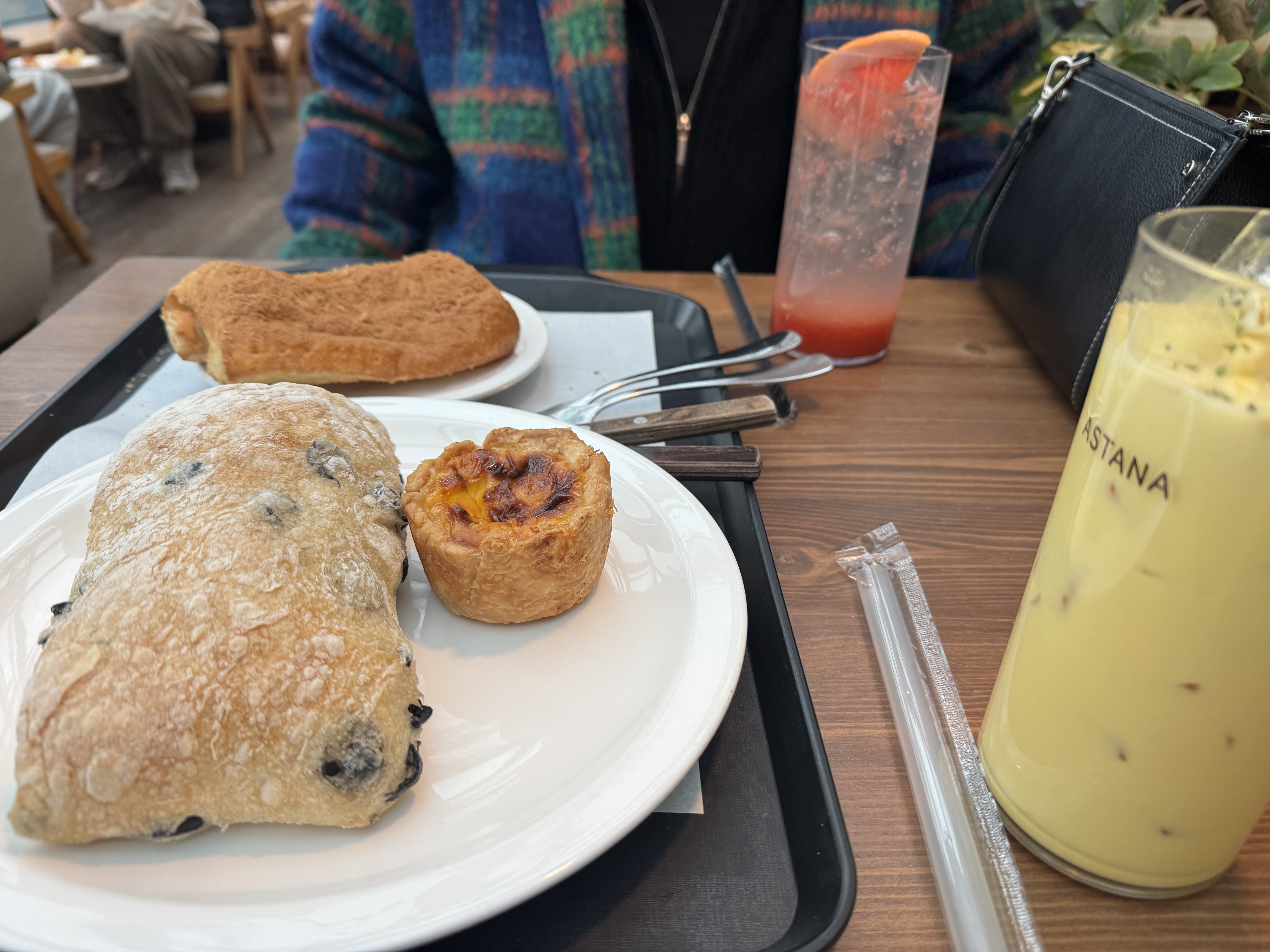 동탄 카페 아스타나에서 주문한 빵과 음료, 올리브가 들어간 담백한 치아바타 스타일 빵과 에그타르트, 시나몬 슈가가 묻은 납작한 빵이 흰 접시에 담겨 있고 옆에는 아이스 옥수수라떼와 자몽에이드가 놓인 테이블 풍경