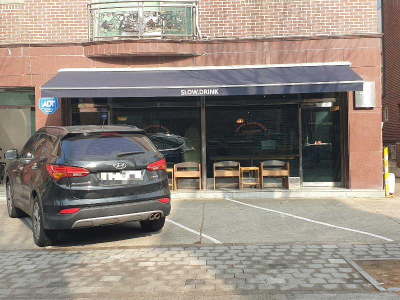 적벽돌로 된 건물에 적색 타일로 꾸며진 카페 외관. 앞 주차장엔 차량 1대가 서있다.