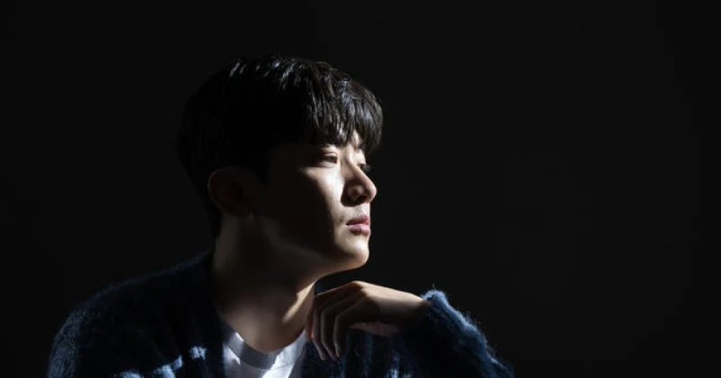 검은 배경으로 가디건을 입고 옆모습을 보여주고 있는 김우진