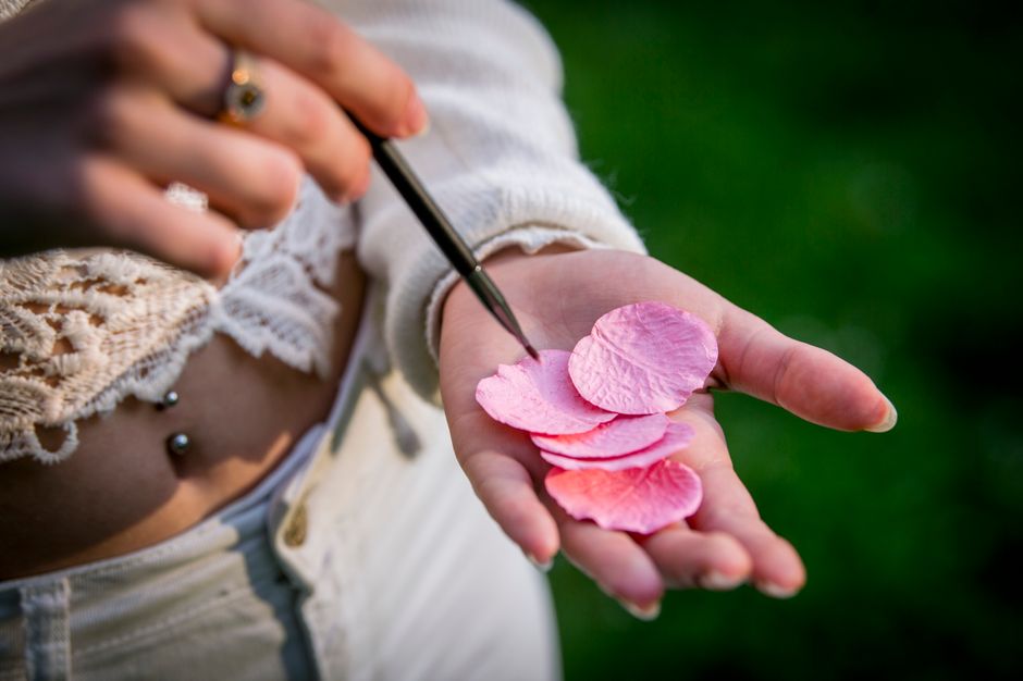 A detailed close-up of a hand holding pink petals, with focus on floral beauty outdoors.