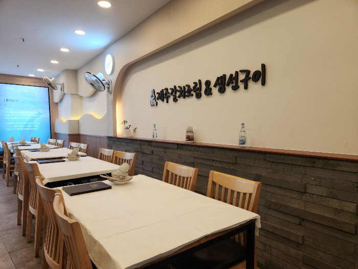 흰 천으로 덮인 테이블과 나무 의자들이 홀 안에 있습니다