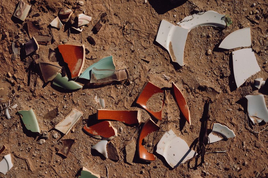 A collection of broken ceramic pieces scattered on a dirt ground under sunlight.