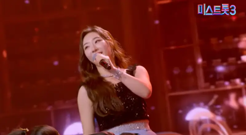 미스트롯3- 빨간배경 앞 검은나시티 긴머리를 늘어뜨린채 왼손에 마이크를 들고 노래하는 곽지은