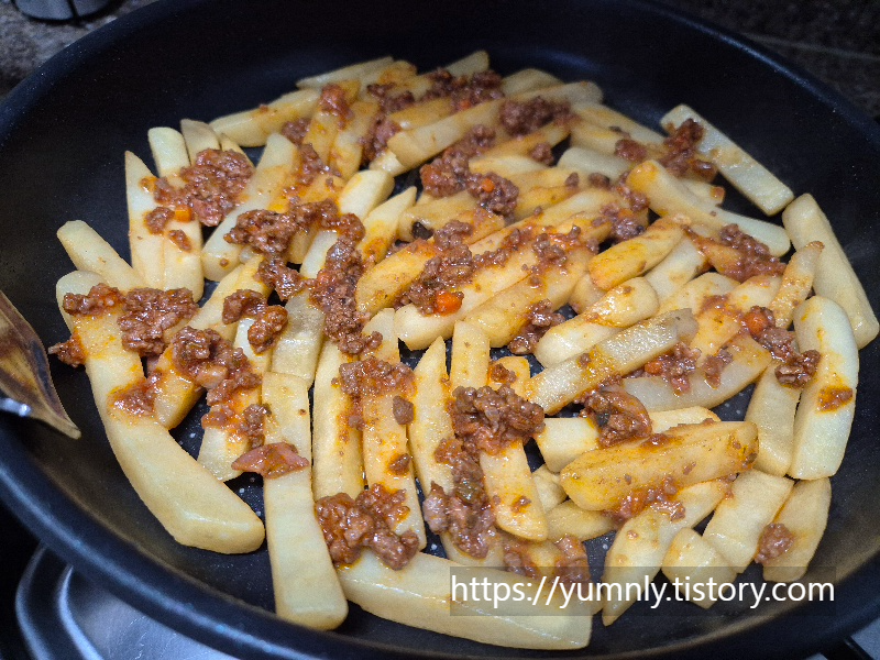 Spreading red ragu sauce over crispy french fries in a pan