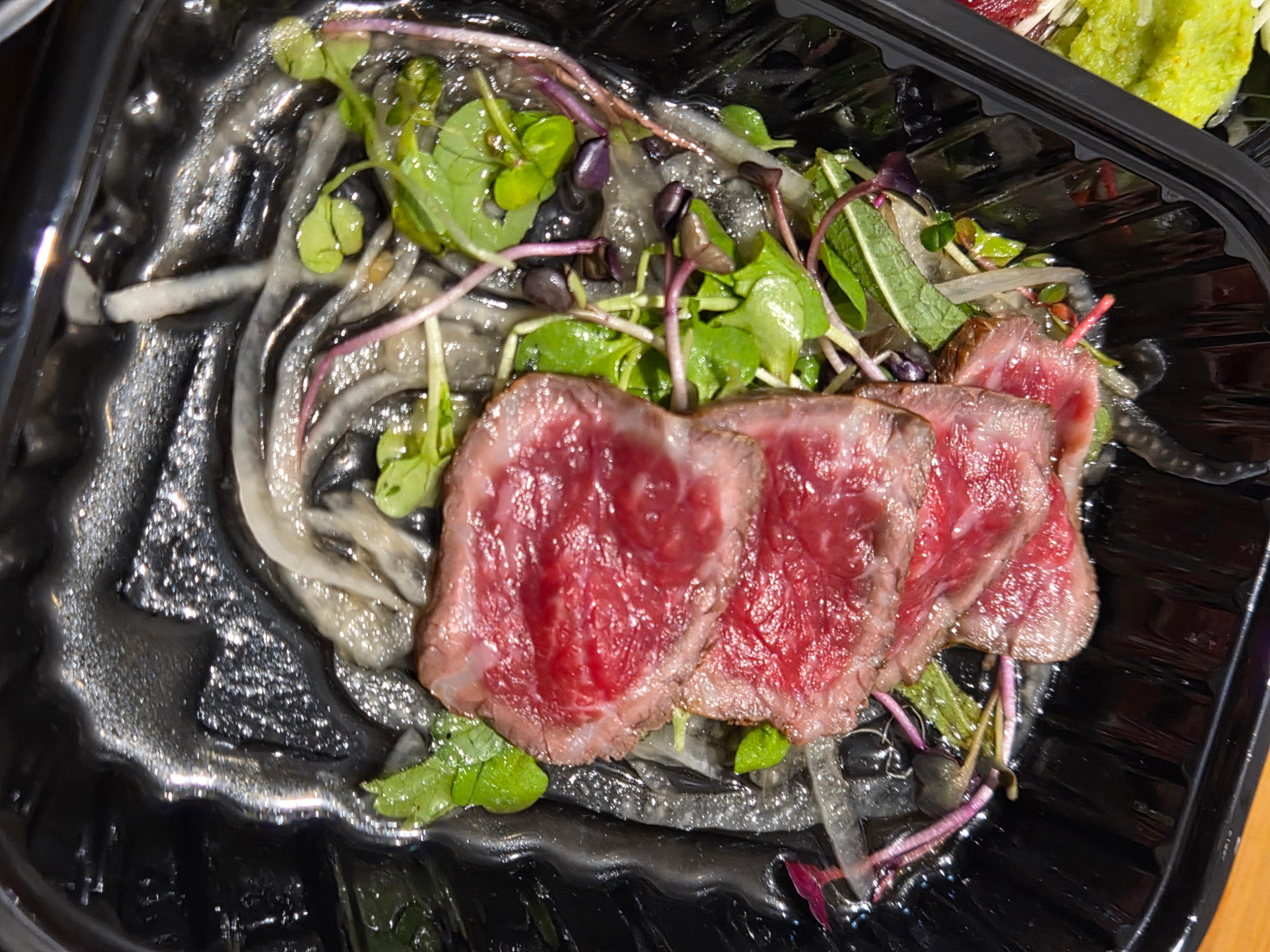 얇게 구워낸 한우 타다끼가 어린잎 채소와 양파 위에 올려져 있는 클로즈업