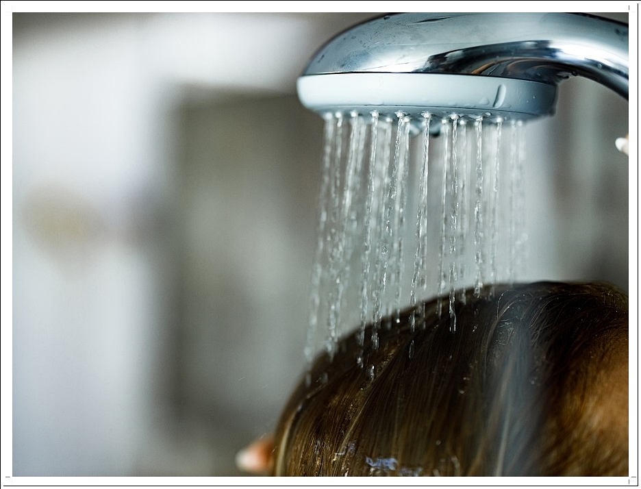 샤워기에서 물이 떨어지고 그 밑에 사람의 머리.