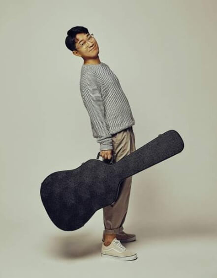 유해준이-기타-케이스를-들고-서서-미소를-짓는-사진