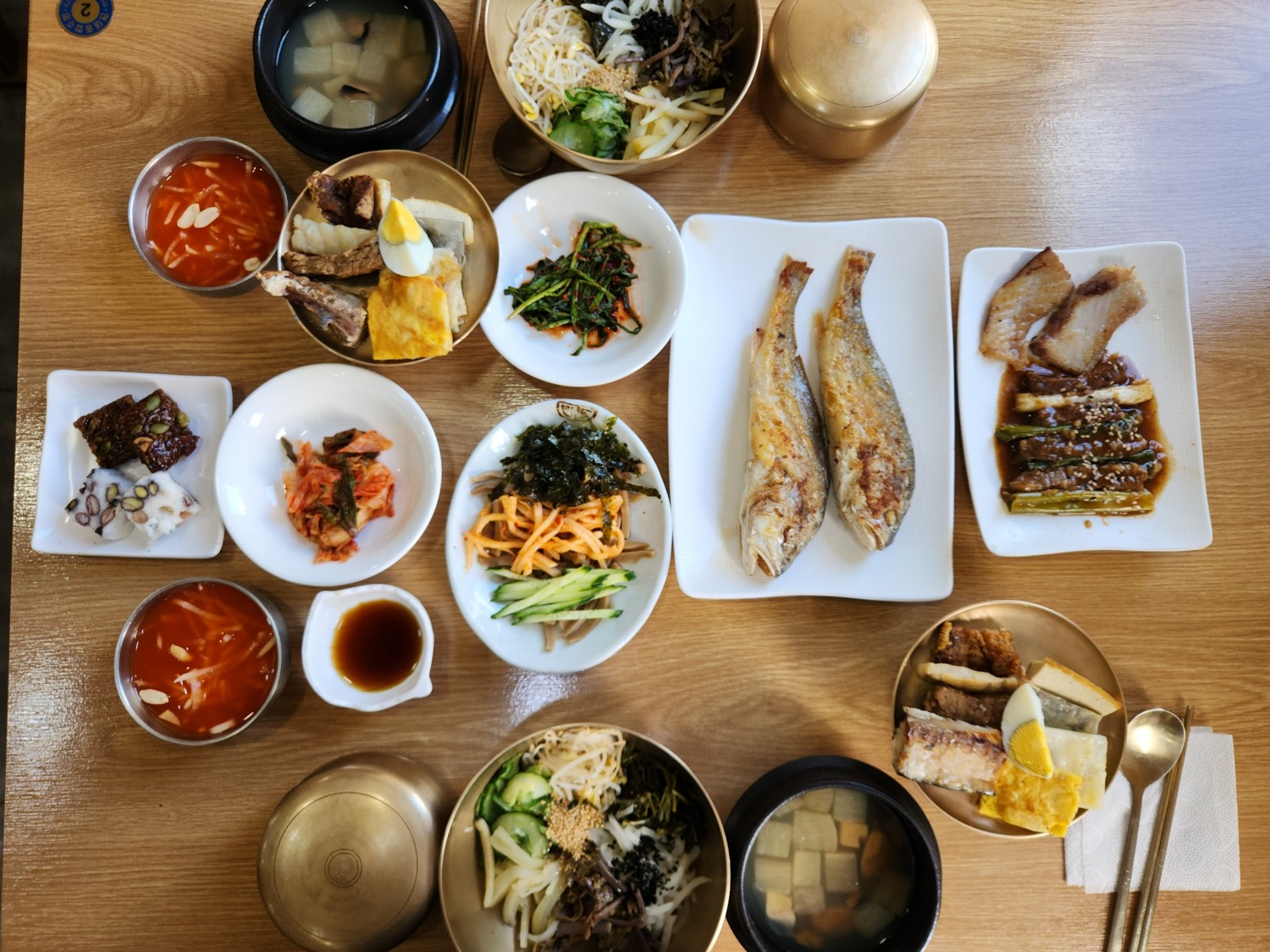 나무 테이블 위에 생선, 김치, 전, 산적, 밥, 국 등이 올려져 있다