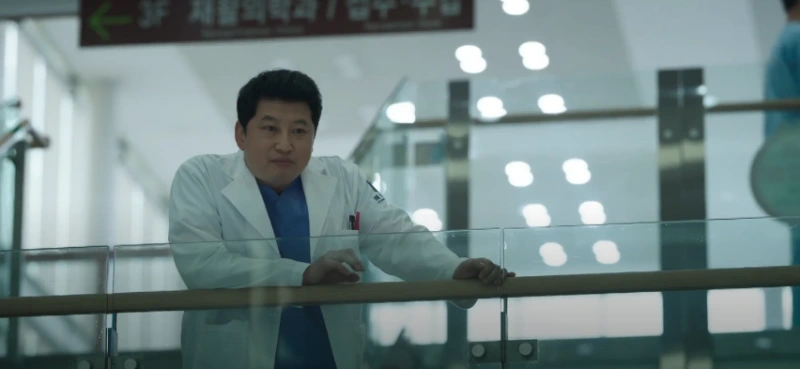 흰 의사 가운을 입고 뱅원 로비 2층 난간에 기대고 있는 드라마 유괴의 날 윤정도 캐릭터