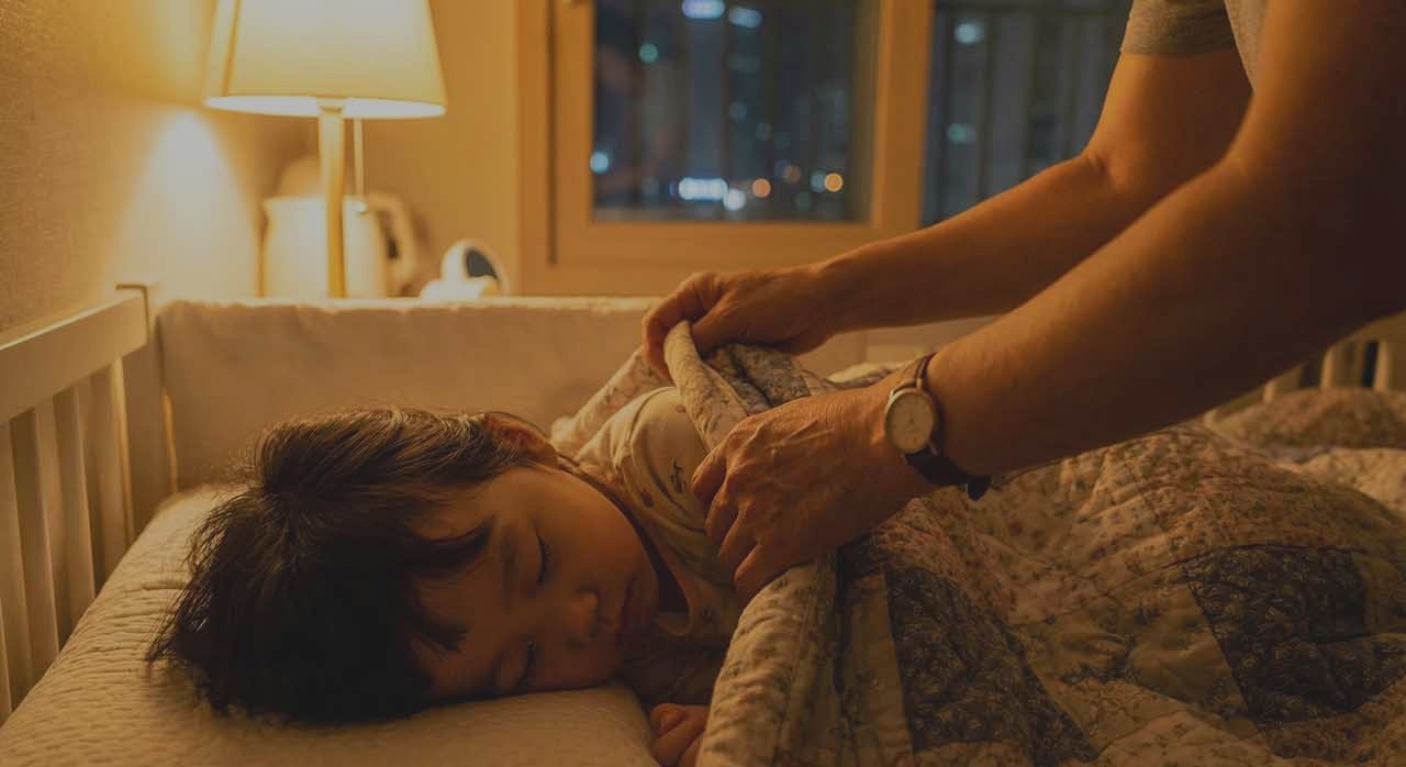 잠든 아이 옆에서 이불을 정리해 주는 보호자의 손 모습이다. [ⓒ이달의건강]