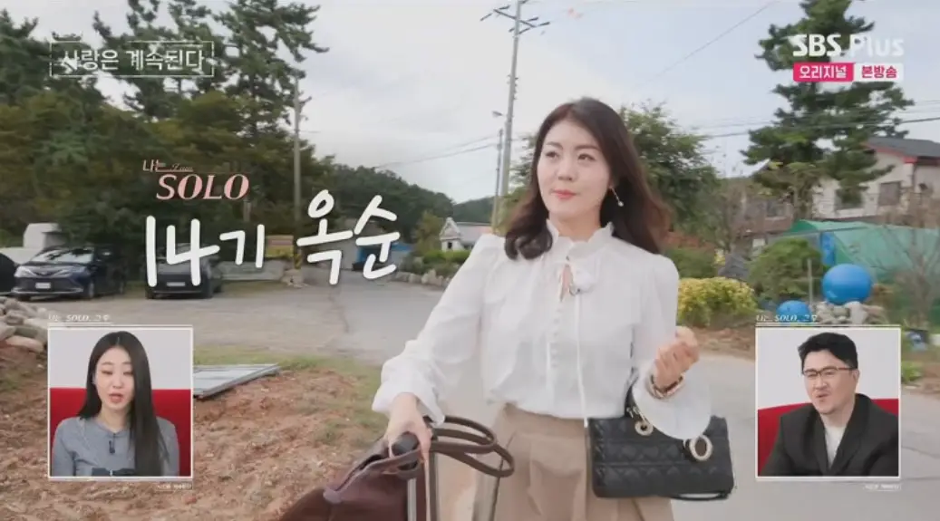 나솔사계-
긴 웨이브머리에 흰블라우스 아이보리색 치마를 입고 검은 검방을 든채 웃으며 걸어가는 여자 14기 옥순