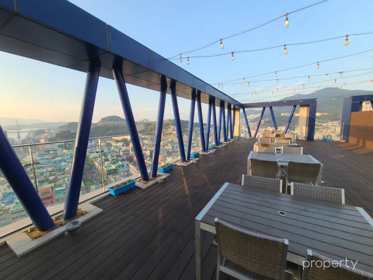 케니호텔루프탑-테이블이여러개있고-위에줄에걸린전구들-유리난간-여수시내전경이보이는