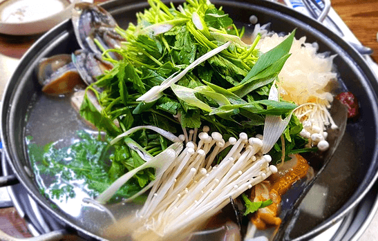 둥그런 냄비 안에 샤브샤브가 가득하다. 국물 위에 하얀 팽이버섯, 조개들, 녹색 채소와 대파가 가득하다.