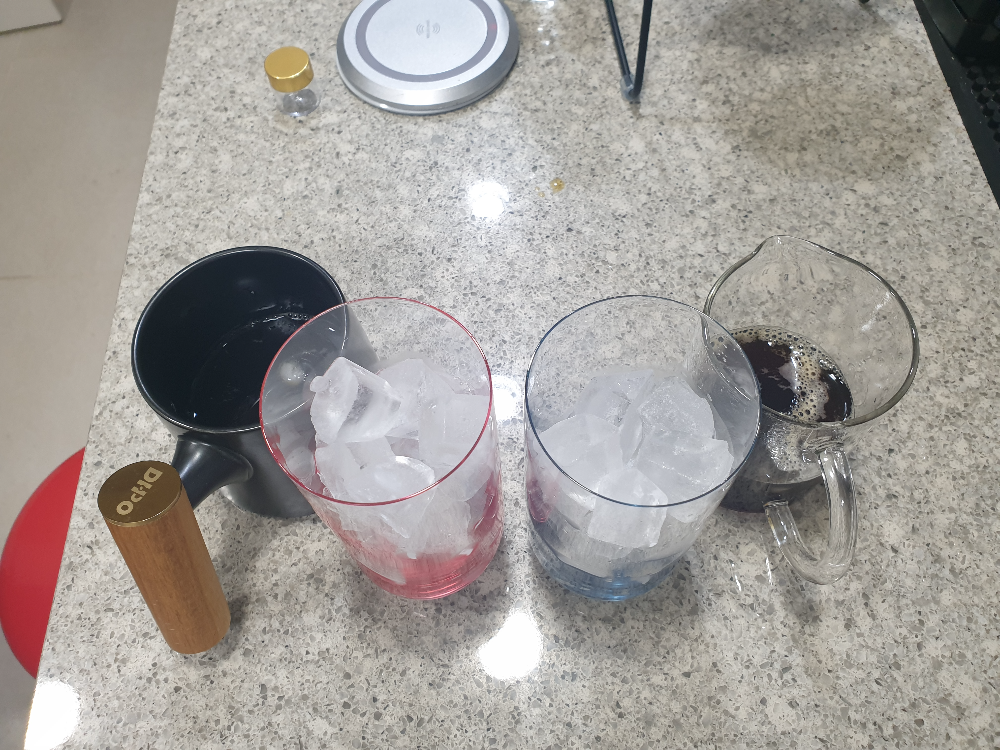 가장 왼쪽부터 커피가 담긴 검은 색 세라믹컵, 얼음이 닮긴 반투명한 붉은색 얼음컵, 얼음이 담긴 불투명 블루컵, 커피가 담긴 비커