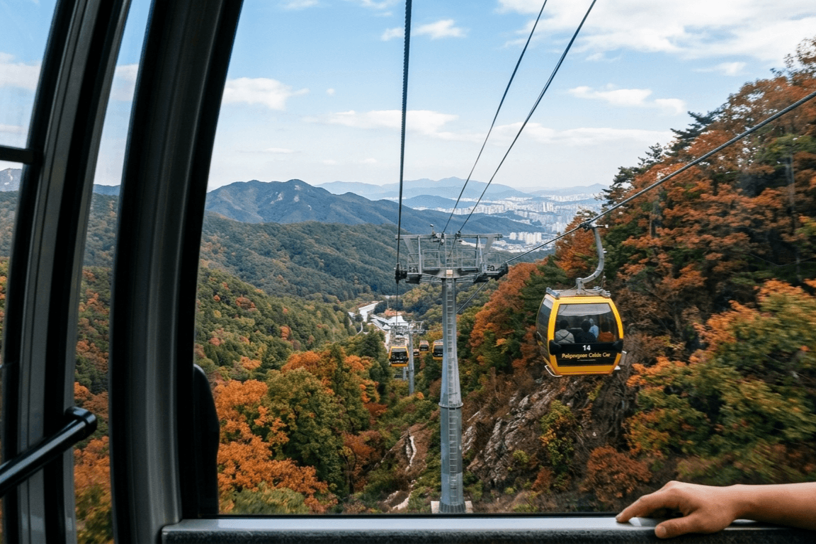 팔공산 케이블카 내부에서 촬영한 가을 단풍 산과 노란 케이블카, 멀리 대구 시내가 보이는 풍경