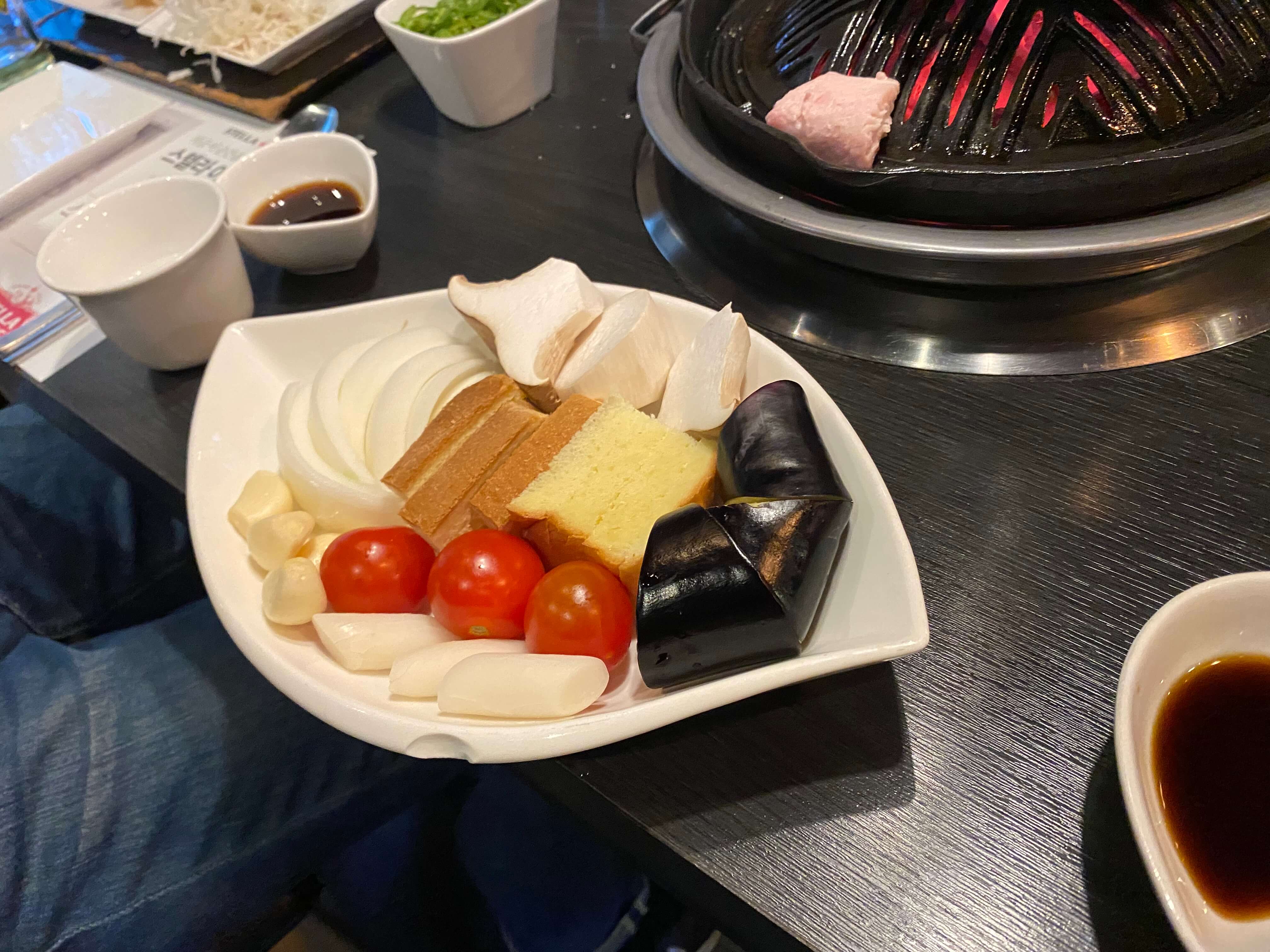 고기와 함께 제공되는 밑반찬과 야채이다. 김치와 각종 나물&amp;#44; 소스가 좌측에 있고 가지&amp;#44; 토마토 양파&amp;#44; 떡 마늘 등이 왼쪽에 있다.