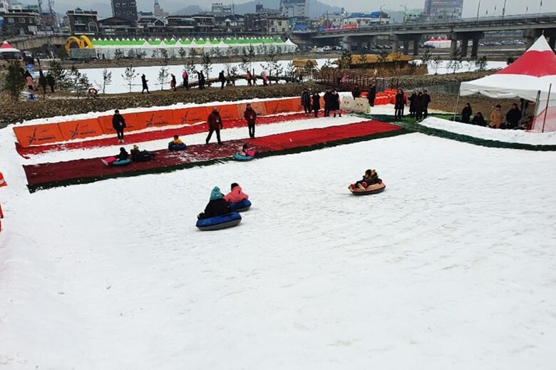 눈썰매장으로 어린아이들이 튜브모양의 썰매를 타고 하얀 눈으로 뒤덮힌 경사진 썰매장에서 아래쪽으로 미끄러져 내려오는 모습과 종착지에서는 안전요원이 대기하고 있는 모습