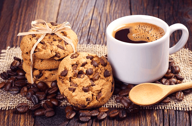 초콜릿 쿠키가 여러개 있고 주변엔 커피콩들이 가득하다. 오른쪽엔 하얀 커피잔에 블랙커피가 있다.