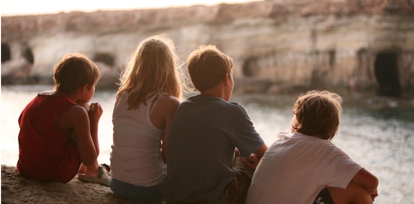 여자어른 1명과 남자 어린이 3명이 강변에 앉아 있는 뒷모습을 찍은 사진
