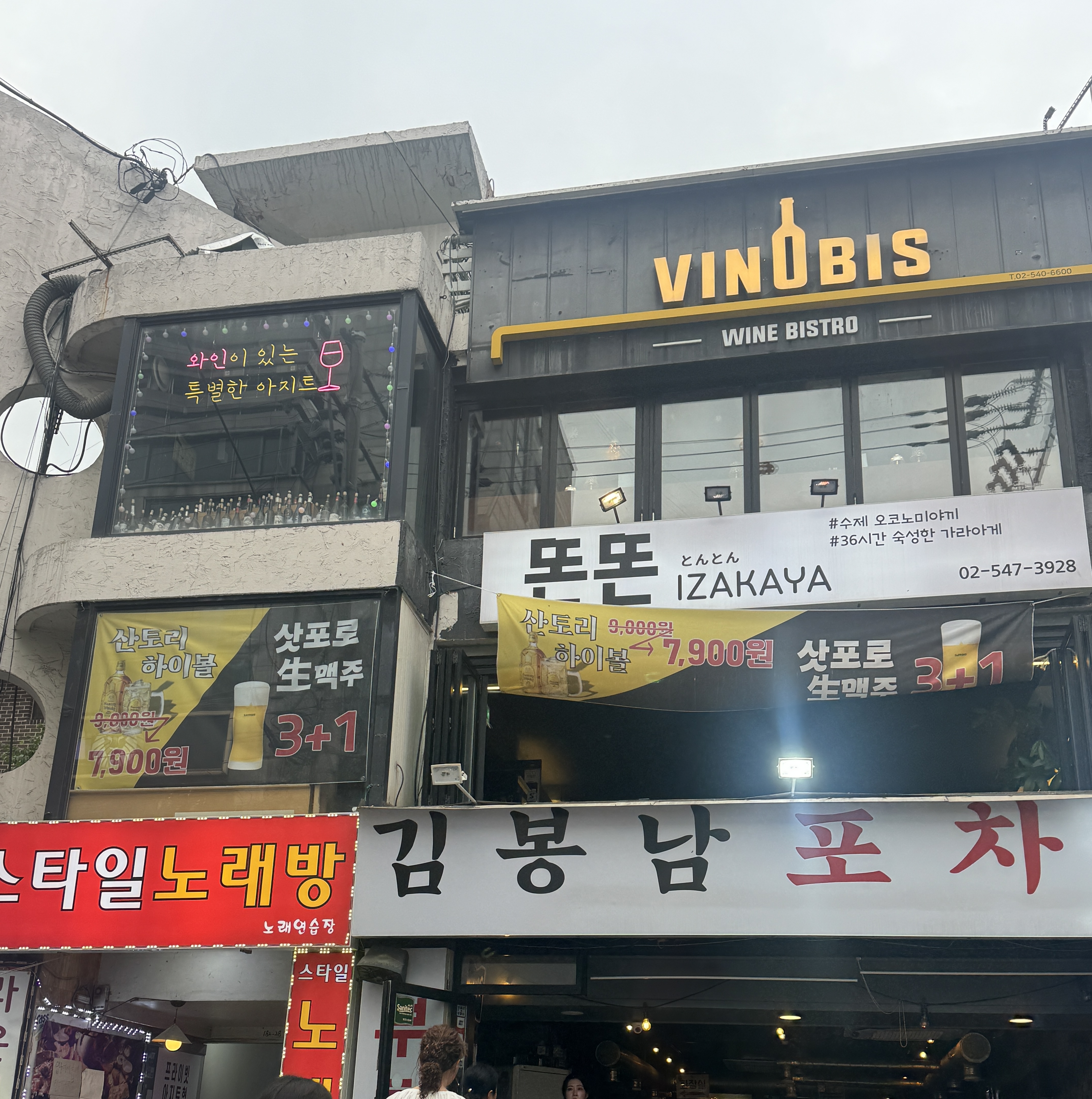 논현동 번화가 속&amp;#44; 간판이 다닥다닥 붙은 건물 3층에 위치한 와인바 Vinobis 외관. 허름한 외관이지만 소박하고 숨겨진 분위기를 암시한다.