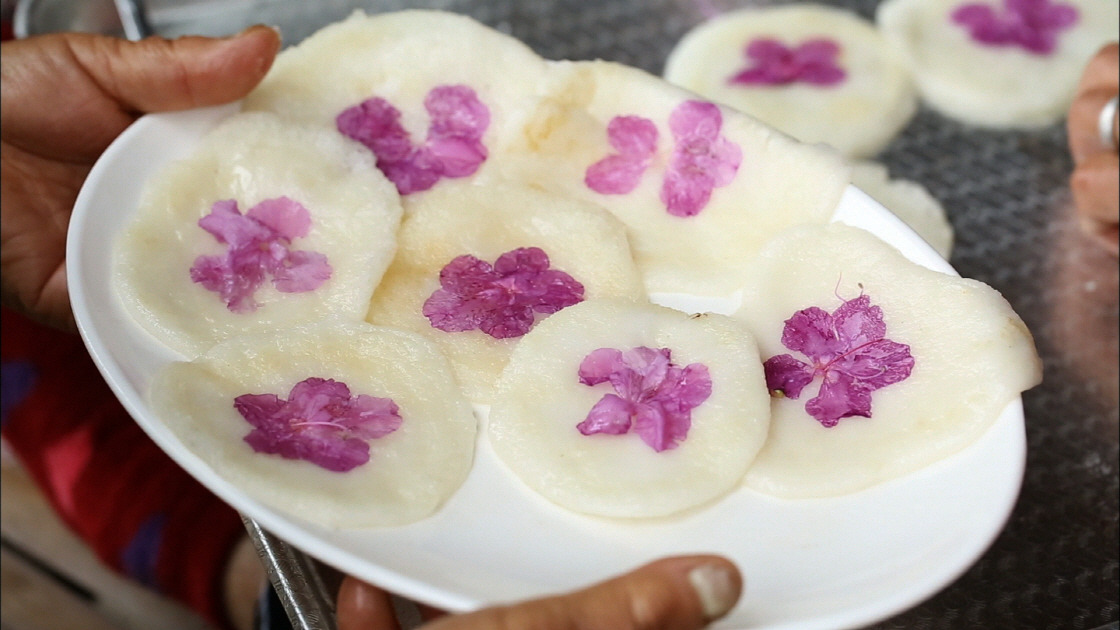 두 손으로 진달래 화전이 담긴 흰 접시를 들고있음