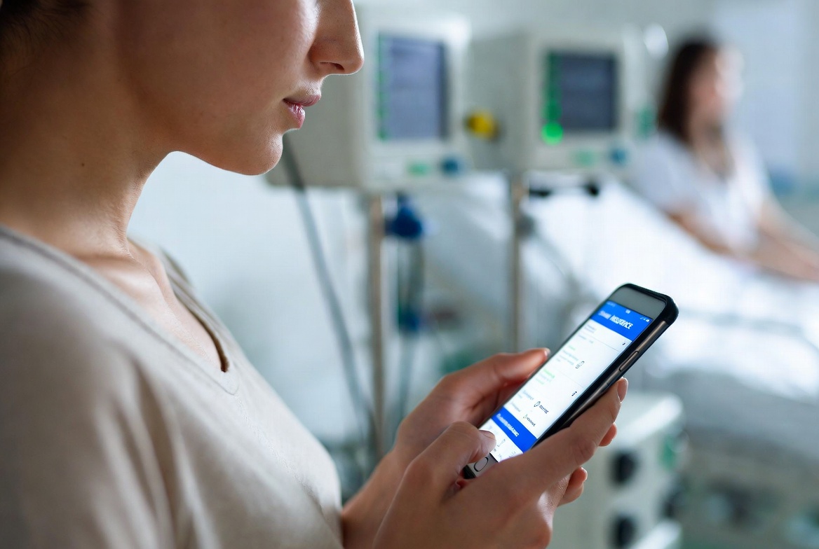 병원 입원실에서 가족(보호자가)이 스마트폰으로 보험앱에 접속해서 보는 이미지