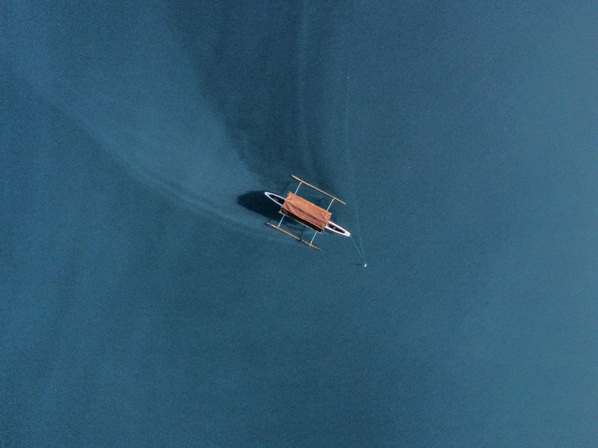 An aerial photo showing a wooden boat floating on tranquil blue waters.