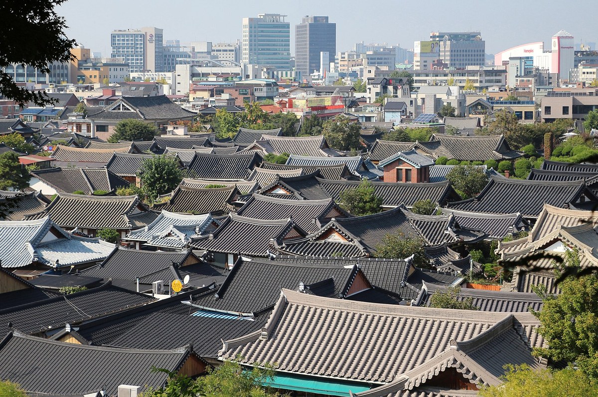 Rows of tiled hanok rooftops in Jeonju Hanok Village with the city of Jeonju behind them