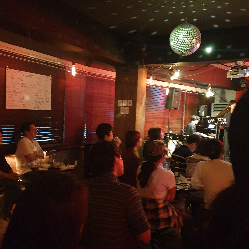 공연 밴드를 향해 앉아있는 사람들 전체적인 조명은 붉은 톤이다.