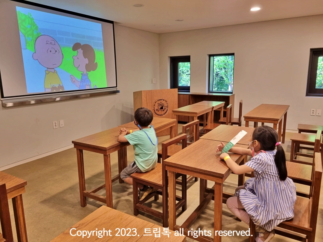 책상에 앉아서 스누피 영상을 보는 아이들