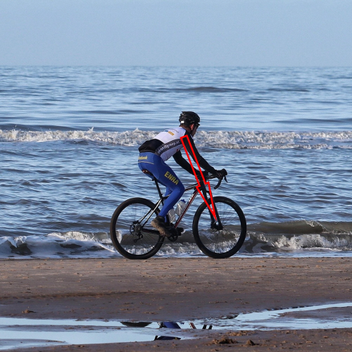 자전거 피팅을 받고 파도가 치는 모래사장 위를 달리고 있다.