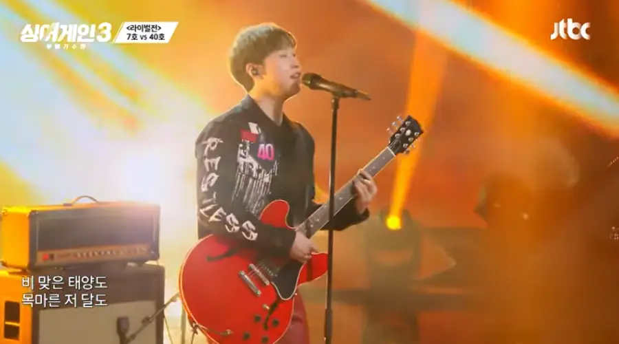 싱어게인3-
황금색 배경 검정색 셔츠에 빨간색 기타를 들고 스탠딩마이크에 대고 노래하는 우측 모습