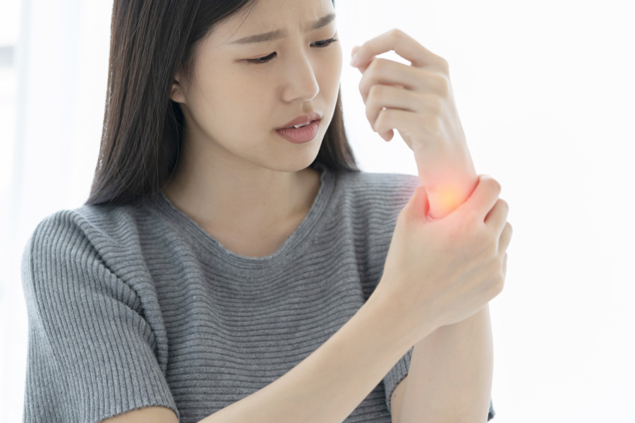 젊은 동양 여성이 본인의 왼쪽 손목의 통증을 억제하기 위해서 오른쪽 손으로 손목을 감싸고 아파하고 있는 것을 찍은 사진