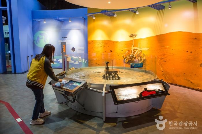 한 여자 아이가 전시관에서 화성 탐사 로봇을 작동하고 있다.