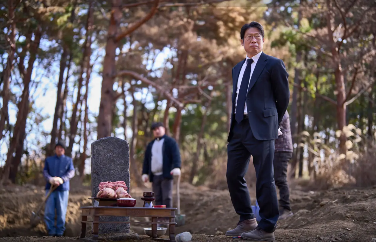 파묘- 산위 나무들 앞 제사상 옆 양복입고 서있는 유해진