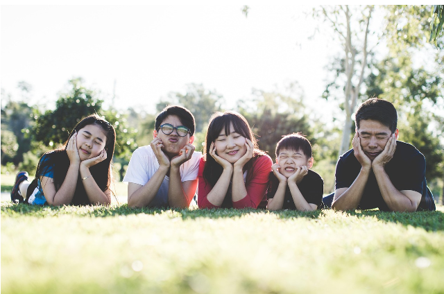 잔디밭에 나란히 누워 환하게 웃고 있는 가족의 모습. 밝은 햇살 아래에서 가족 구성원 모두가 여유롭고 행복한 시간을 보내고 있다.