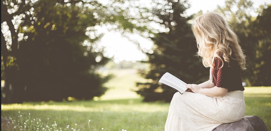 긴 머리의 아름다운 여인이 들판 바위에 걸터앉아 책을 읽고 있는 사진