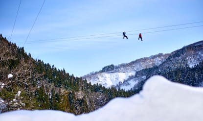 사람 두명이 눈밭위에 있는 얇은 선에 매달려 있다