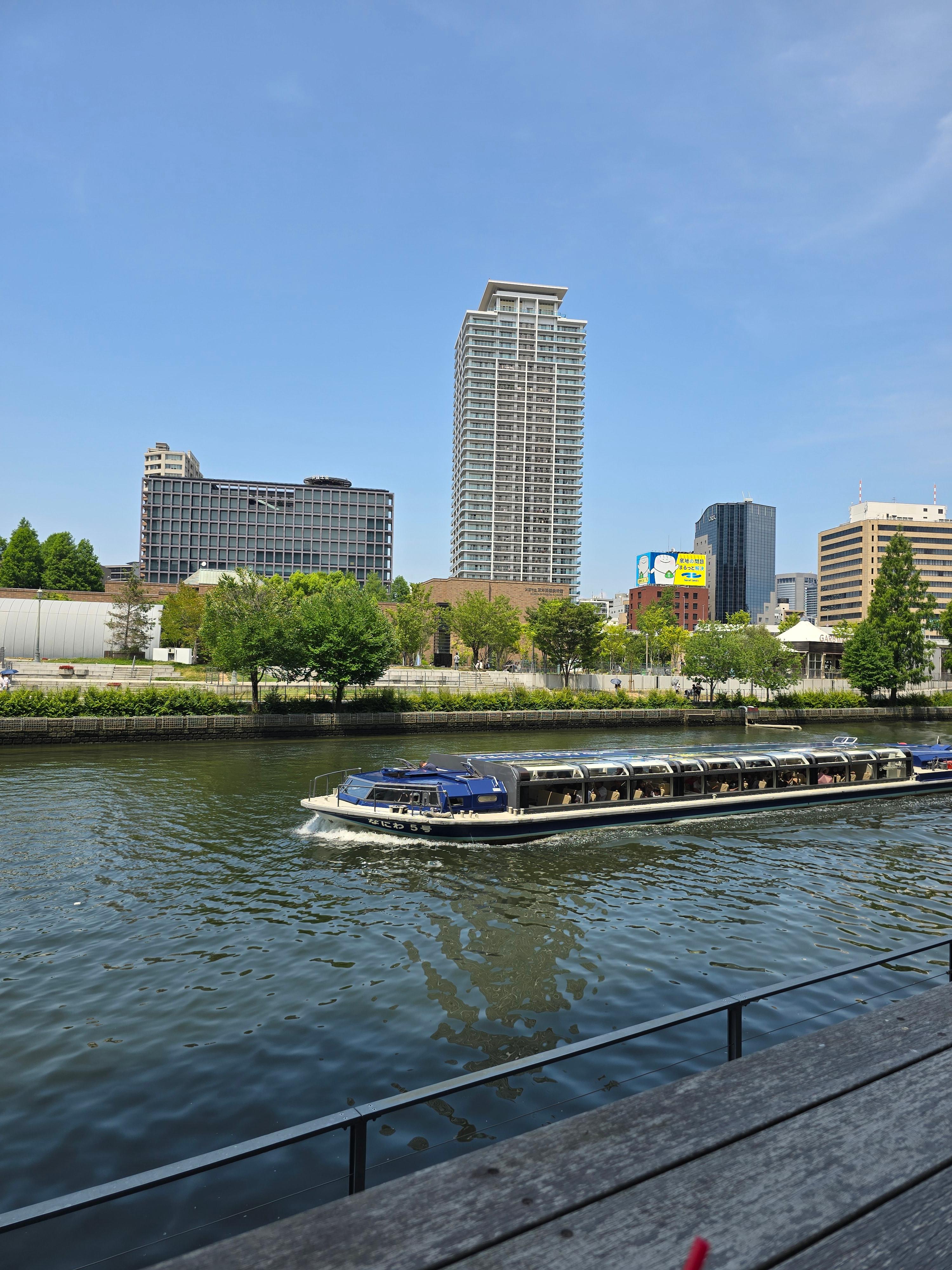 강 위를 천천히 지나가는 유람선과 오사카 중앙공회당이 보이는 강변 풍경