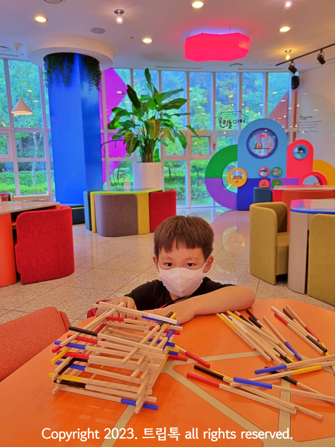 알록달록한 의자들과 주황색 테이블 위에 산가지로 탑을 쌓고 있다.