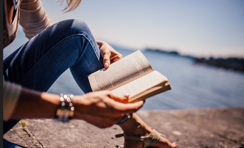 해변에 앉아 독서하는 여인의 모습과 책이 보이는 사진